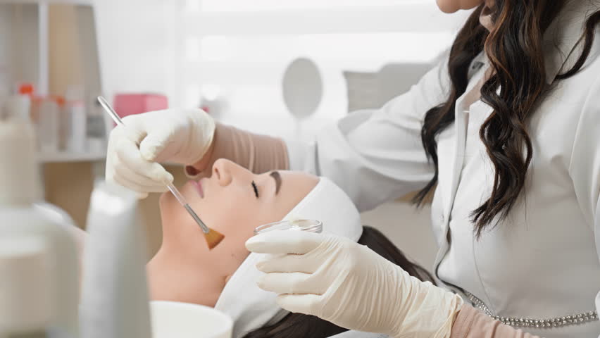The beautician demonstrates professional skills during the facial peeling procedure. In the beauty clinic, a young woman rests and relaxes during a cosmetic peeling procedure. Side view Royalty-Free Stock Footage #1104594329
