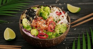Person eating poke with chopsticks, taking a bite of salmon fish cubes, poke bowl with avocado and edamame beans served in coconut bowl, hd video clip, close up 4k horizontal footage