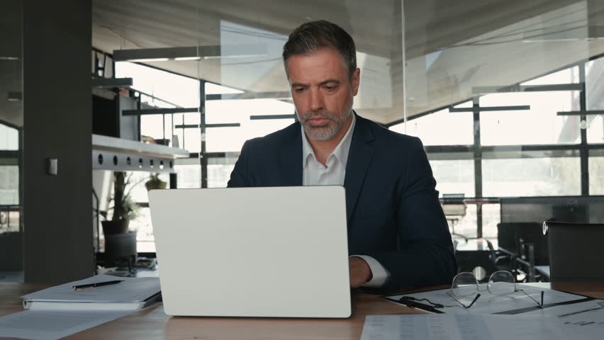 Busy mid aged business man ceo executive investor wearing suit looking at laptop computer analyzing financial data, managing corporate risks, thinking over project strategy solution working in office. Royalty-Free Stock Footage #1104603483