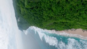 Vertical video. Fpv drone dynamic flight close to mountain cliff rock jungle greenery sea ocean beach coastline wave water aerial view. Exotic wood forest cliff rock island travel tropical lagoon bay