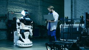 Serviceman with a laptop is observing a modern robot. Human and robot communication concept. - Powered by Shutterstock - Get 15% off with code: PIKWIZARD15