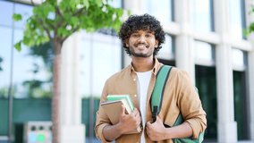 Portrait of smiling university student holding books, textbooks, looking at camera while standing in the campus space near the university building. Happy male with backpack preparing for exam period - Powered by Shutterstock - Get 15% off with code: PIKWIZARD15