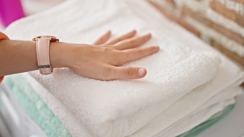 Young beautiful hispanic woman touching folded towels at laundry room
