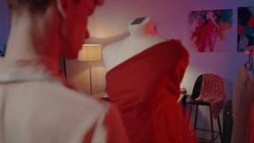Rear view of a creative stylish male tailor taking measures using a centimeter while creating red elegant exclusive dress, pinned on a mannequin in a fashion design workshop, sewing, tailoring atelier