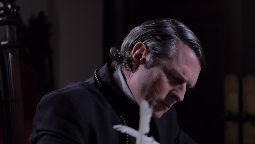 VIRGINIA - SPRING 2023 - Reenactment, Tabletop, quill writing, dipping ink and writing by candle light  by window in a church setting.  Hands of a man with Priest cassock writing at table with quill. Royalty-Free Stock Footage #1104620201