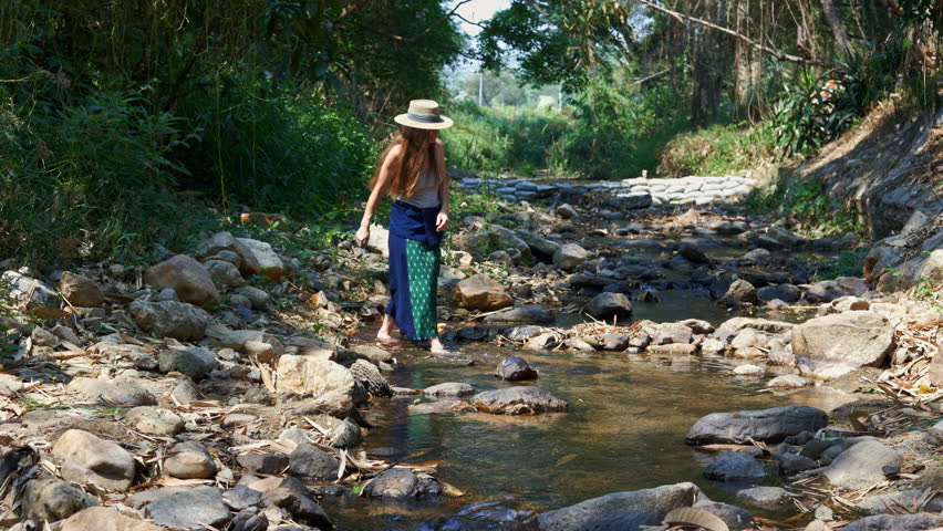 A youthful lady enjoys herself, strolling in the stream while whimsically assuming the role of a fashion show participant.