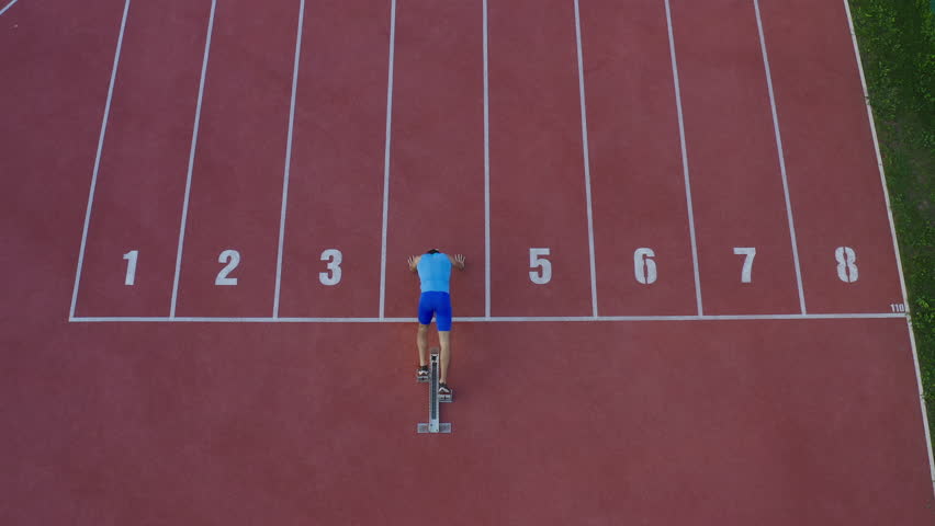 Caucasian male sprint runner alone on the athletic track, taking starting position and running in line four, aerial above shot. - Powered by Shutterstock - Get 15% off with code: PIKWIZARD15