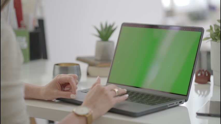 Woman typing on laptop computer on desk with blank chromakey green screen. Home office, working from home, website application or webshop, for selling product online. Royalty-Free Stock Footage #1104628233