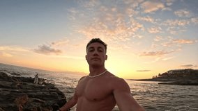 One attractive and happy young man at the beach smiling and looking at the camera holding and taking a selfie with his phone. Summer time in vacation holiday at the sunset
