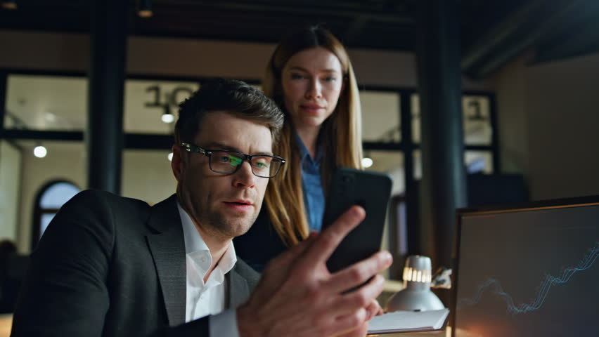 Business team working late looking smartphone. Friendly colleagues check mobile phone data discuss sales project at workplace. Two trading brokers smiling professionals together. Busy finance managers Royalty-Free Stock Footage #1104632447