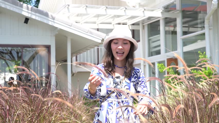 Asian woman in tourist hat taking a walk in the middle of the meadow in the summer wind blowing in front of a cafe