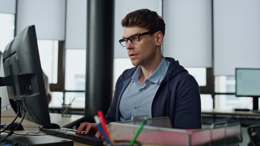 Thoughtful programmer looking computer at desk. Focused it man analysing code searching problem solution in office. Professional software engineer type keyboard creating application. Serious coder guy Royalty-Free Stock Footage #1104643615