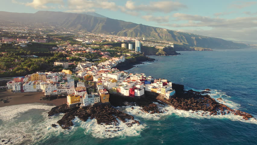 Aerial view of the beautiful colourful oceanside town of Punta Bravo at sunrise, Tenerife, Canary Islands, Spain. Drone orbit shot. Tenerife coastal town near Puerta de la Cruz, Spain Royalty-Free Stock Footage #1104644763