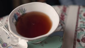 Top down shot of pouring milk into a beautiful floral patterned tea cup with tea in it. Close up