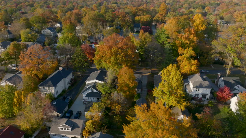 Aerial over gorgeous trees at peak color and beautiful houses in the Kirkwood neighborhood of St. Louis, Missouri on a beautiful day in Autumn.