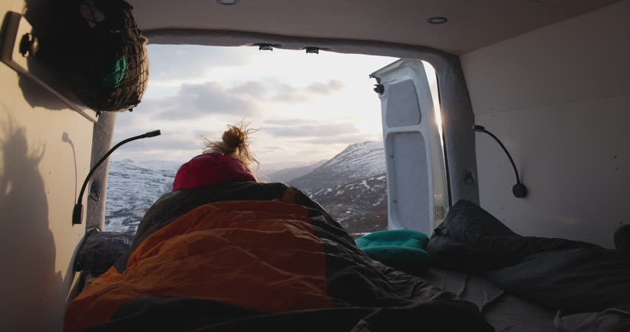 Female watch Norway mountain sunset from campervan in sleeping bag; reveal