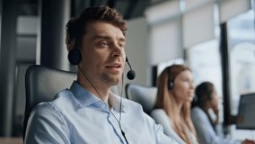 Smiling man working telemarketing center. Friendly man manager consult client in headphones. Professional support agent assistant talking typing keyboard helping customer. Hotline conversation concept - Powered by Shutterstock - Get 15% off with code: PIKWIZARD15