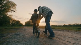 Dad teaches his son to ride a two-wheeled bicycle at sunset on a field road. - Powered by Shutterstock - Get 15% off with code: PIKWIZARD15