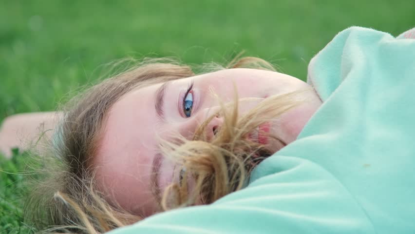 Young Caucasian Girl Relaxing Laying on Her Back on Green Grass Lawn
