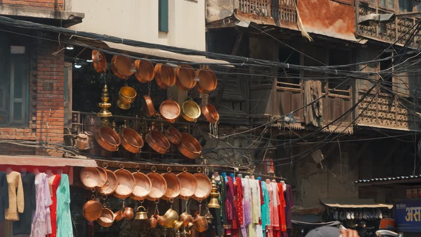 marketplace vendor selling brass prayer pots tilts up towards kathmandu apartments