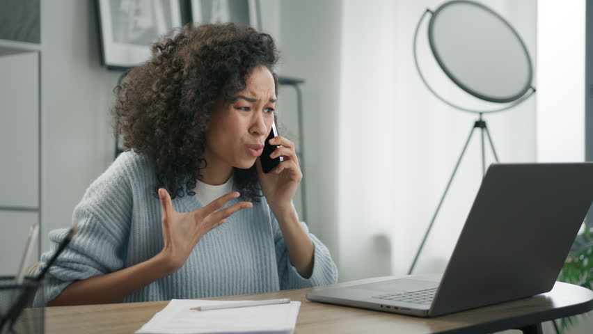 Displeased emotional woman of color looking at laptop screen, dissatisfied with bad news yelling NO at phone 4K. Unhappy stressed african american female mobile user hearing bad news by smartphone Royalty-Free Stock Footage #1104654457
