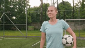 A portrait of a female football player training on a mini-football stadium. The girl holds a ball in her hand, looks into the camera, and smiles. - Powered by Shutterstock - Get 15% off with code: PIKWIZARD15