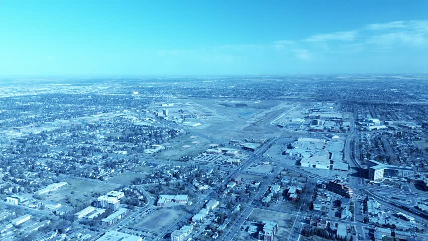 aerial drone flyover deserted airfield airport runway in major city on a sunny summer day next to empty commercial hangars shopping mall low rise buildings surrounding property formerly known as YEG