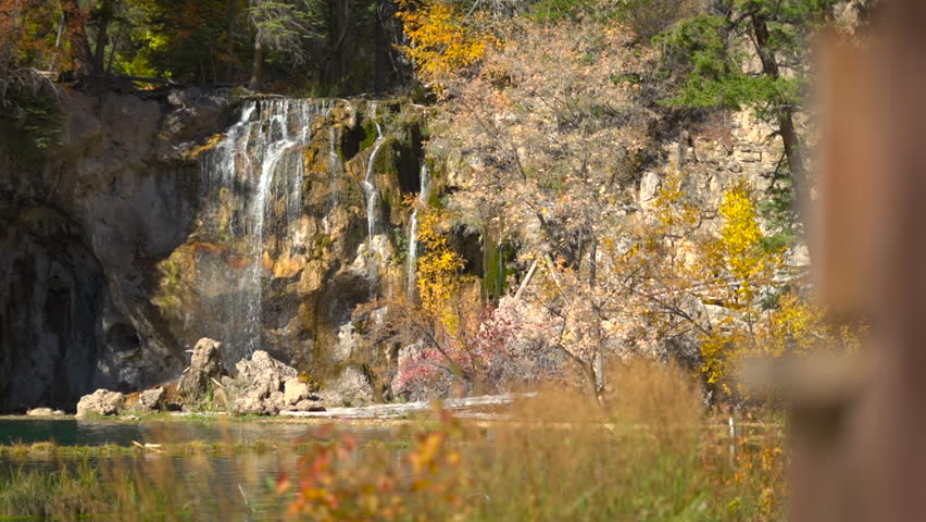 Pan across foreground reeds reveals mossy waterfall cascade of Hanging Lake, Colorado