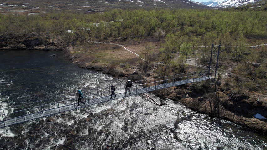 Three Hikers Walking over a Suspension Bridge on the Kungsleden near Abiskojaure in The Swedish Mountains, Backpacking in the Forest, Pan from Right ot Left