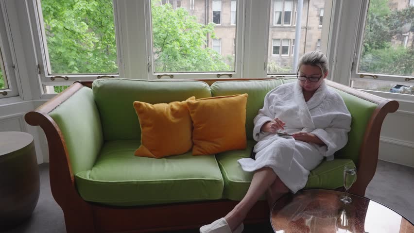 Couple wearing white dressing gowns sit down on a sofa to chat, locked off