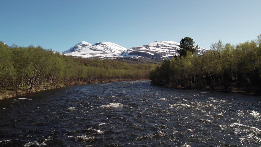 Aerial View of Stunning Serene Swedish River with Mountains full of Snow in the Background, Summer on the Kungsleden in the Abisko National Park, Drone Hovering over the River
