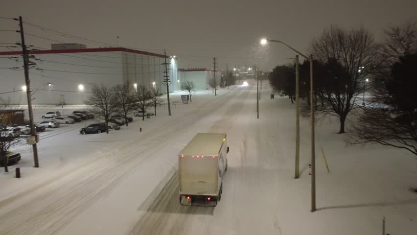 Brampton , Canada - 02 21 2023: Aerial tracking follow semi truck driving through snowy road at night