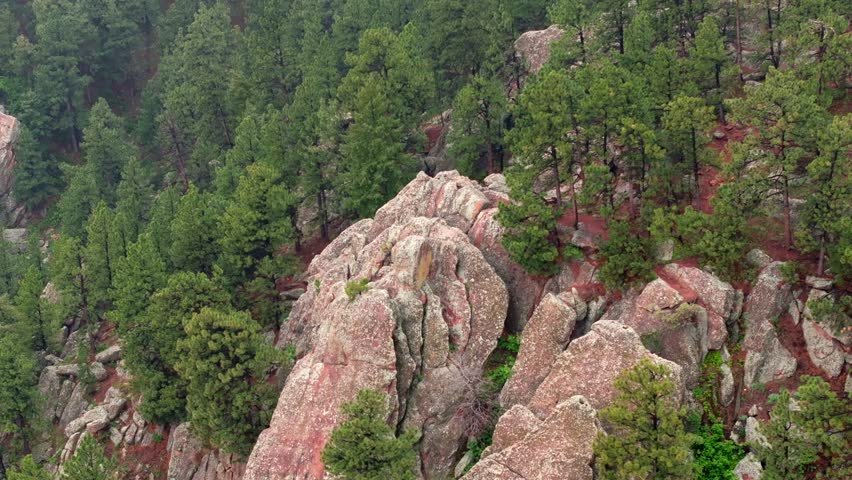 Rock formation in the Rocky Mountains with pine trees surrounding. Aerial pull back establishing shot.