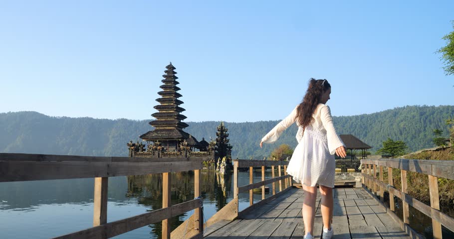 Traveling woman or influencer enjoying her trip through Bali indonesia in front of a historic temple Pura Segara Ulun Danu Batur in the water at volcanic lake batur the Pura Ulun Danu temple Royalty-Free Stock Footage #1104661843
