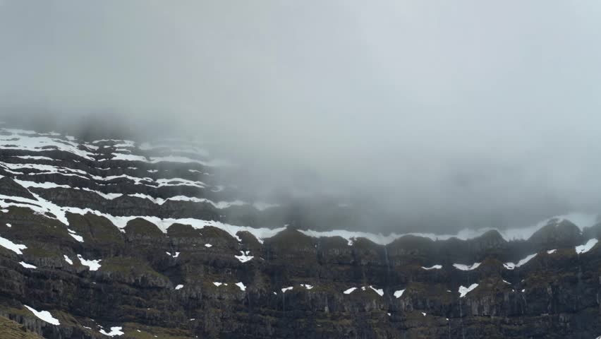Time lapse of flying grey clouds around snowy mountain on Faroe island