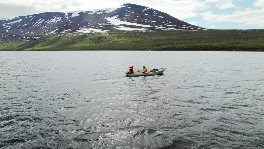 Aerial Lateral Drone Shot of a Young Couple Crossing a Lake by Rowing a Boat in the Swedish Mountains, Kungsleden Trail, Teusajaure Mountain Cabin