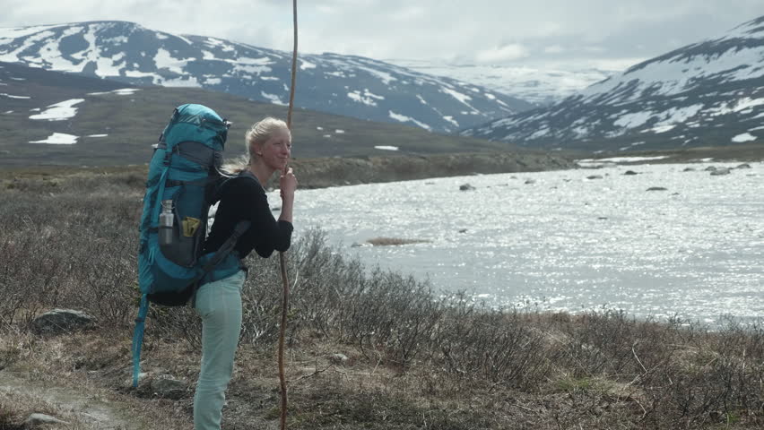 Young Blond Female Hiker Standing at a River in the Swedish Mountains on the Kungsleden Trail, Enjoying the Sun and the Wind on Her Face