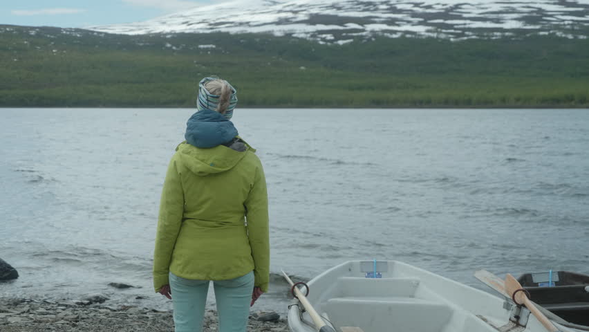 Girl standing by The Lake in the Swedish Mountains, Girl trying to cross the lake by boat, Kungsleden Trail, Teusajaure Mountain Cabin