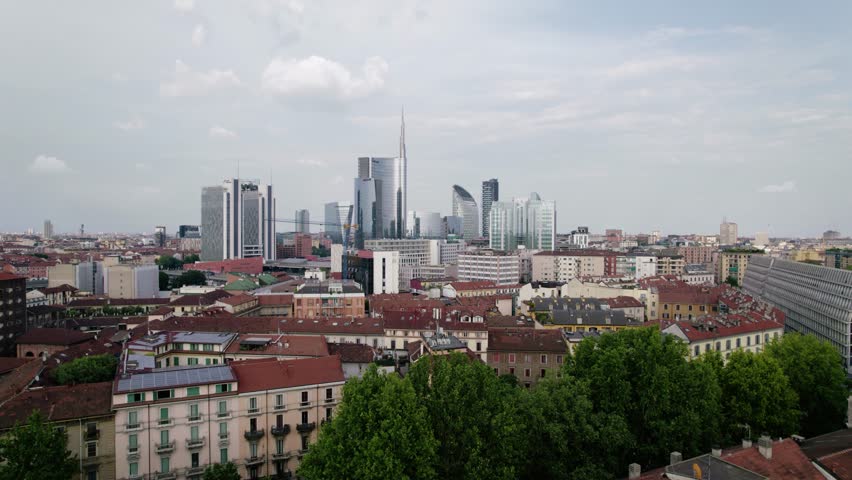 Aerial view of skyscrapers towering over the city of Milan, Italy. Contrast between modern and historical buildings. Camera moves backwards. Nobody inside.