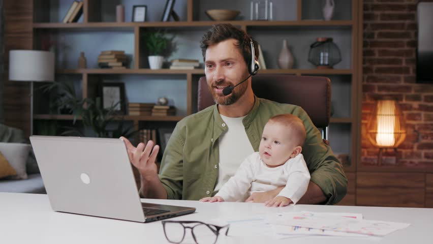 Father on maternity leave, holding an online conference, a meeting in the home office with a small child in his arms. Dad with a child. Freelancer combines child care and work. Paternity leave Royalty-Free Stock Footage #1104663845