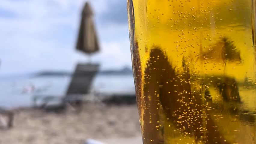 Beer bubbles, close-up. Enjoying a cold glass of blond beer at the beach at summer, bubbles moving up. Blank glass perfect for adviertisment, logo, text, marketing. Royalty-Free Stock Footage #1104664163