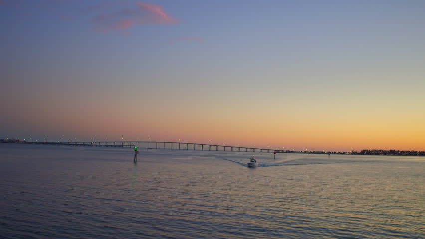 Aerial Shot Of Motorboat On Sea Near Bridge Against Orange Sky, Drone Ascending Forward At Dusk - Miami, Florida