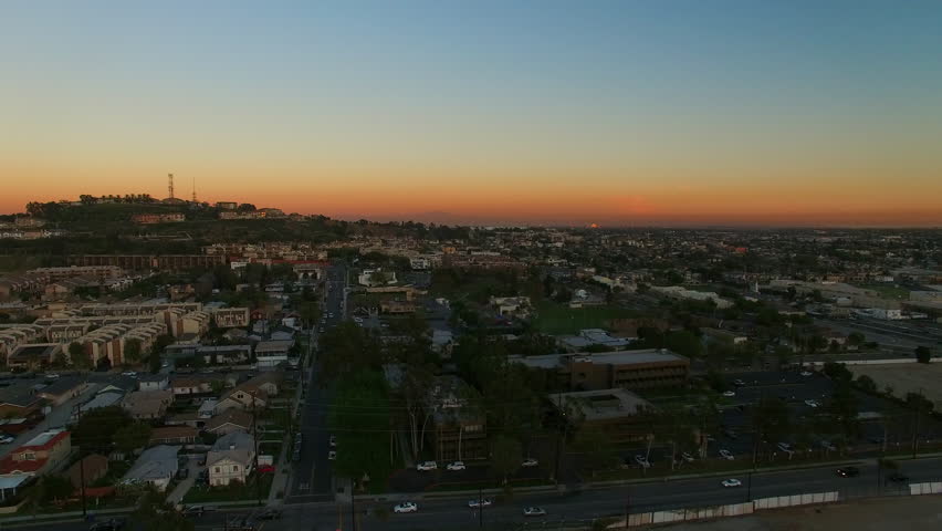 Aerial Shot Of Suburb Near Hill Against Orange Sky At Dusk, Drone Flying Backward Over Neighborhood In City - Long Beach, California