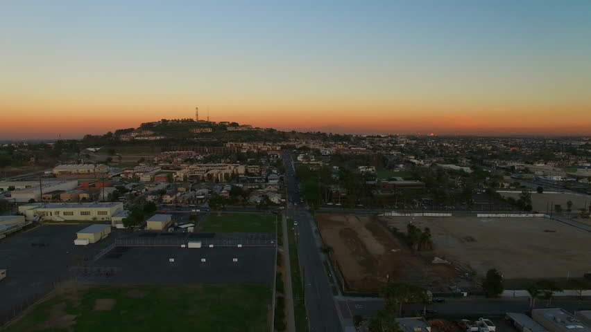 Aerial Shot Of Suburb Near Hill Against Orange Sky At Dusk, Drone Flying Forward Over Neighborhood In City - Long Beach, California