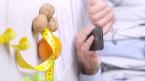 Vertical video of Nutritionist doctor with smartphone and Walnuts, orange and measure tape on Table
