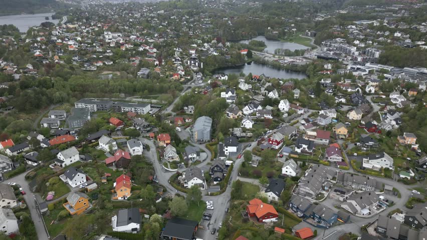 Suburban Expensive Neighbourhood with Traffic and Nesttun Center in the Background. Aerial drone slow panning shot on a cloudy day.