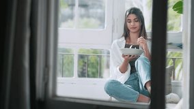 Video of young relaxing woman eating healthy salad while sitting on couch in the living room full of plants at home
