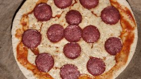 Black pepper sprinkles on pizza, seasoning. Pizza salami, ham, cheese. Freshly baked salami ham pizza with cheese. Spins beautifully. Video clip. Pizza smiley.
