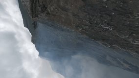 Vertical video 4k. Aerial view flight over volcanic vent sharp ridge with crater smoke mist fog mountain valley. FPV sport drone shot scenic volcano geology formation cliff texture fumes gas hot steam
