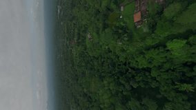 Vertical video. Aerial view picturesque Asian village jungle landscape panorama with house touristic hotel building. FPV sport drone shot exotic rural countryside scenery tropical mountains cloud sky
